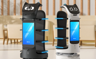 Zwei Bella Bot Roboter mit Bildschirmen auf ihren Oberteilen stehen zusammen und wirken freundlich und einladend.