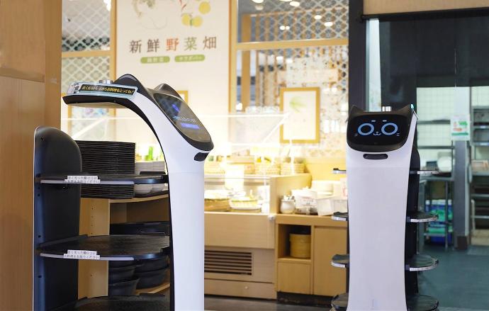 Two Pudu service robots, BellaBot, serve food in a restaurant.