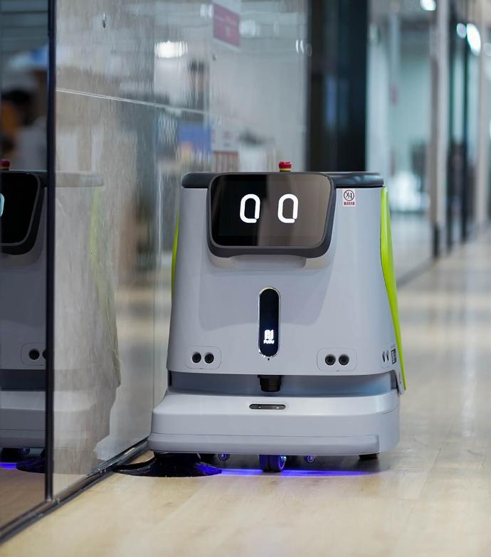 Bild des Pudu Robotics CC1 Reinigungsroboters, ausgezeichnet mit dem Red Dot Award 2023, in Grau mit leuchtend grünen Akzenten und einem freundlichen Gesichtsausdruck.
