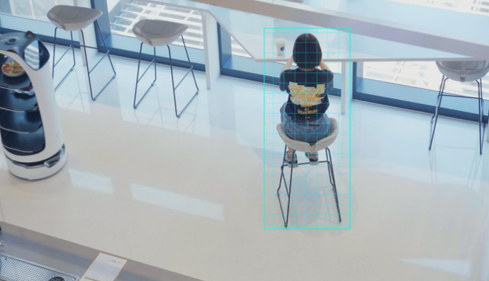 Der Pudu BellaBot-Roboter steht im Raum, während eine Person auf einem Stuhl steht.